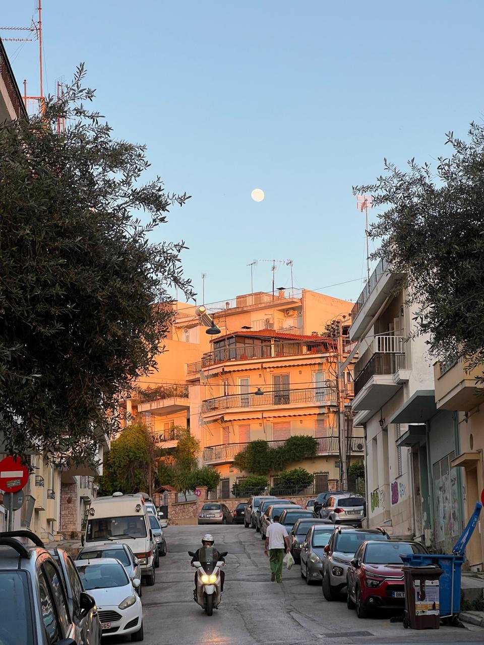 pangrati street at dusk with the full moon rising over the rooftops